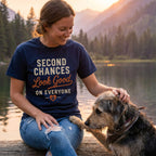 Woman wearing a navy blue cotton t-shirt with Second Chances Look Good on Everyone text, sitting by a lake with a dog.