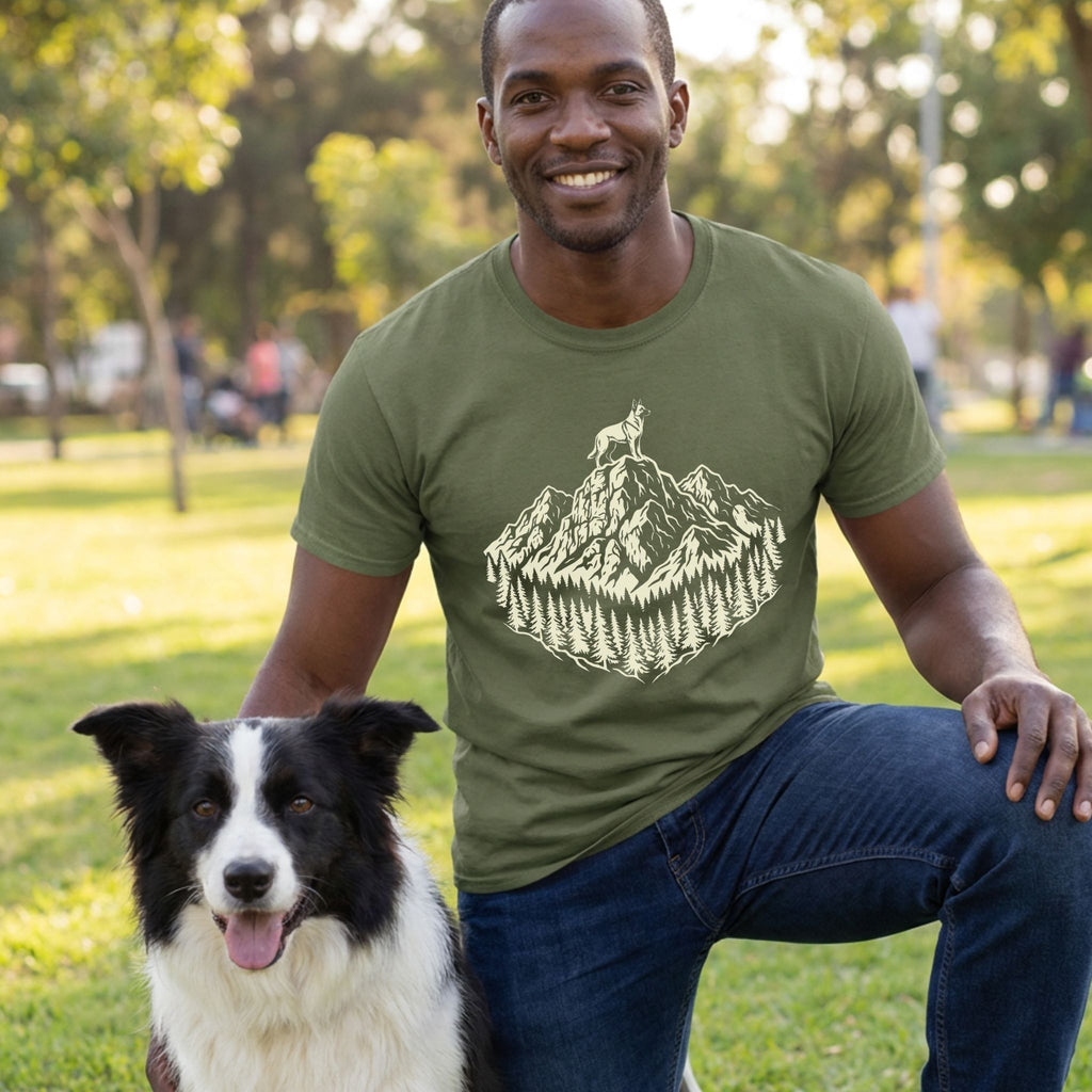 Man in an olive green "King of The Hill" t-shirt with a mountain and dog graphic, kneeling beside a Border Collie.