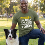 Man in an olive green "Talking To The Dog" t-shirt kneeling next to a black and white border collie.