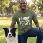 Man in an olive green "Fragile Handle With Treats" t-shirt kneeling next to a black and white dog.