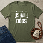 Olive green "Easily Distracted By Dogs" t-shirt with white text, folded jeans, and a dog treat bag.