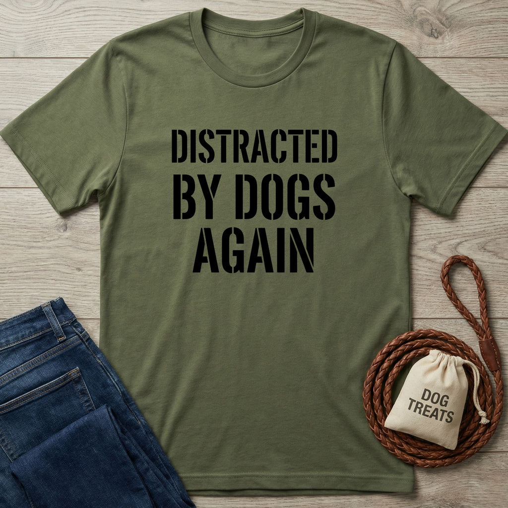 Olive green Gildan Softstyle® t-shirt with "DISTRACTED BY DOGS AGAIN" in black text, next to jeans and dog treats.