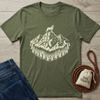 Olive green cotton t-shirt with a cream graphic of a dog on a mountain peak surrounded by pine trees.