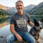 Man in a charcoal grey "I Like Dogs Most People Are OK Too" tee with a blue heeler by a mountain lake.