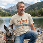Man wearing a beige crewneck t-shirt with My Dog Is My Social Circle text, sitting by a lake with his cattle dog.