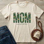 Cream Gildan Softstyle® t-shirt with "MOM nurtured with love" in floral green print, beside jeans and dog treats.