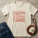Cream Gildan Softstyle t-shirt with "Cozy Vibes & Canine Cuddles" in red script, beside jeans and dog treats.