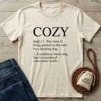 Cream Gildan Softstyle® t-shirt with "COZY" definition print, next to blue jeans and a dog treat bag.