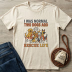 Cream "Normal Two Dogs Ago Rescue Life" t-shirt with dog illustrations, next to jeans and a treat bag.