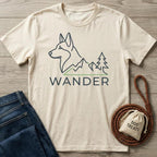 Cream Wander Dog T-shirt with husky, mountains, and tree graphic, beside jeans and dog treats.