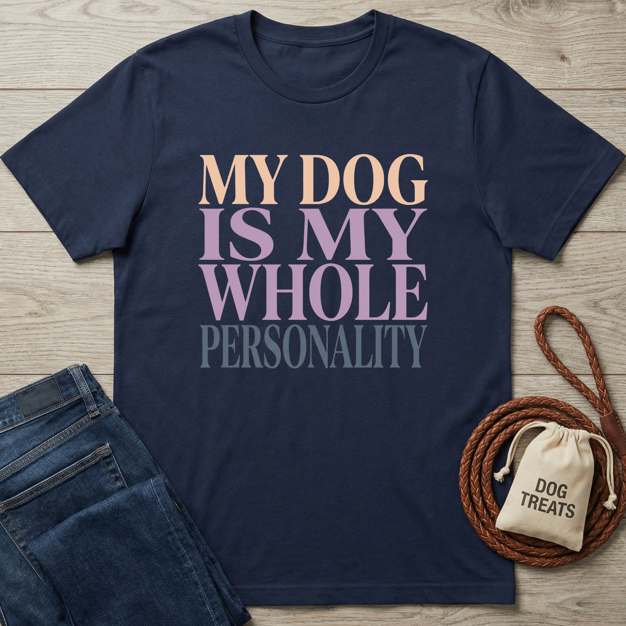 Navy cotton t-shirt with "My Dog Is My Whole Personality" in pastel text, next to jeans and dog treats bag.