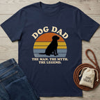 Navy blue "Dog Dad" t-shirt with a black dog silhouette against a sunset, next to jeans and dog treats.