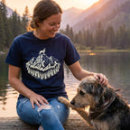 Woman in a navy blue "King of The Hill" t-shirt with a white mountain and wolf design, petting a dog.