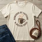 Cream Gildan Softstyle t-shirt with "Powered By Caffeine & Rescue Dogs" graphic, next to jeans and dog treats.