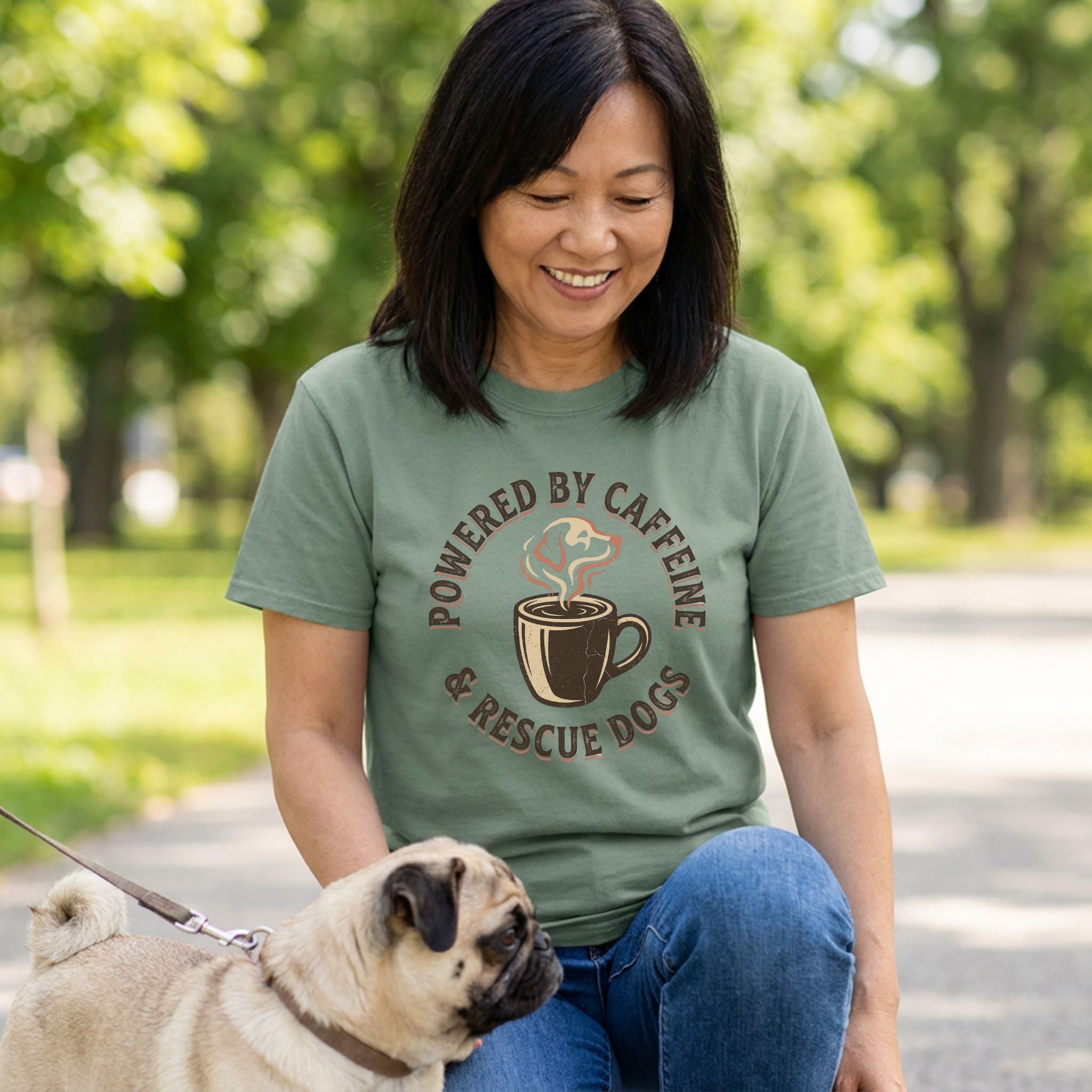 Woman in an sage green "Powered By Caffeine & Rescue Dogs" t-shirt with a pug.