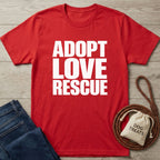 Red Gildan Softstyle® 64000 t-shirt with "ADOPT LOVE RESCUE" in white, next to jeans, dog treats, and a leash.