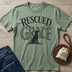 Sage green crewneck t-shirt featuring a black dog graphic and Rescued By Grace typography on a wooden background.
