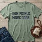 Sage green "Less People. More Dogs." t-shirt with jeans, dog leash, and treat bag on wood.