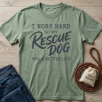 Sage green cotton t-shirt with "I Work Hard So My Rescue Dog Has A Better Life" text, next to jeans and dog treats.