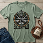 Sage green t-shirt with a compass design featuring a fluffy dog, mountains, and trees.