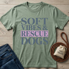 Sage green Gildan Softstyle t-shirt with "SOFT VIBES & RESCUE DOGS" text, next to jeans and dog accessories.