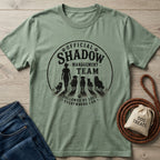 Sage green cotton t-shirt with "Official Shadow Management Team" graphic featuring a person and five dogs.