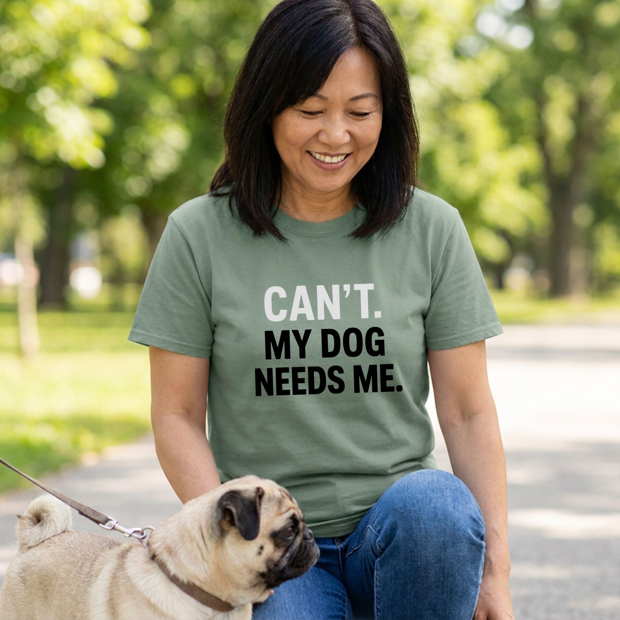 Woman in an olive green "Can't. My Dog Needs Me." t-shirt with a pug.