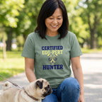 Woman in a green "Certified Egg-Pert Hunter" t-shirt with a dog wearing bunny ears, next to a pug.