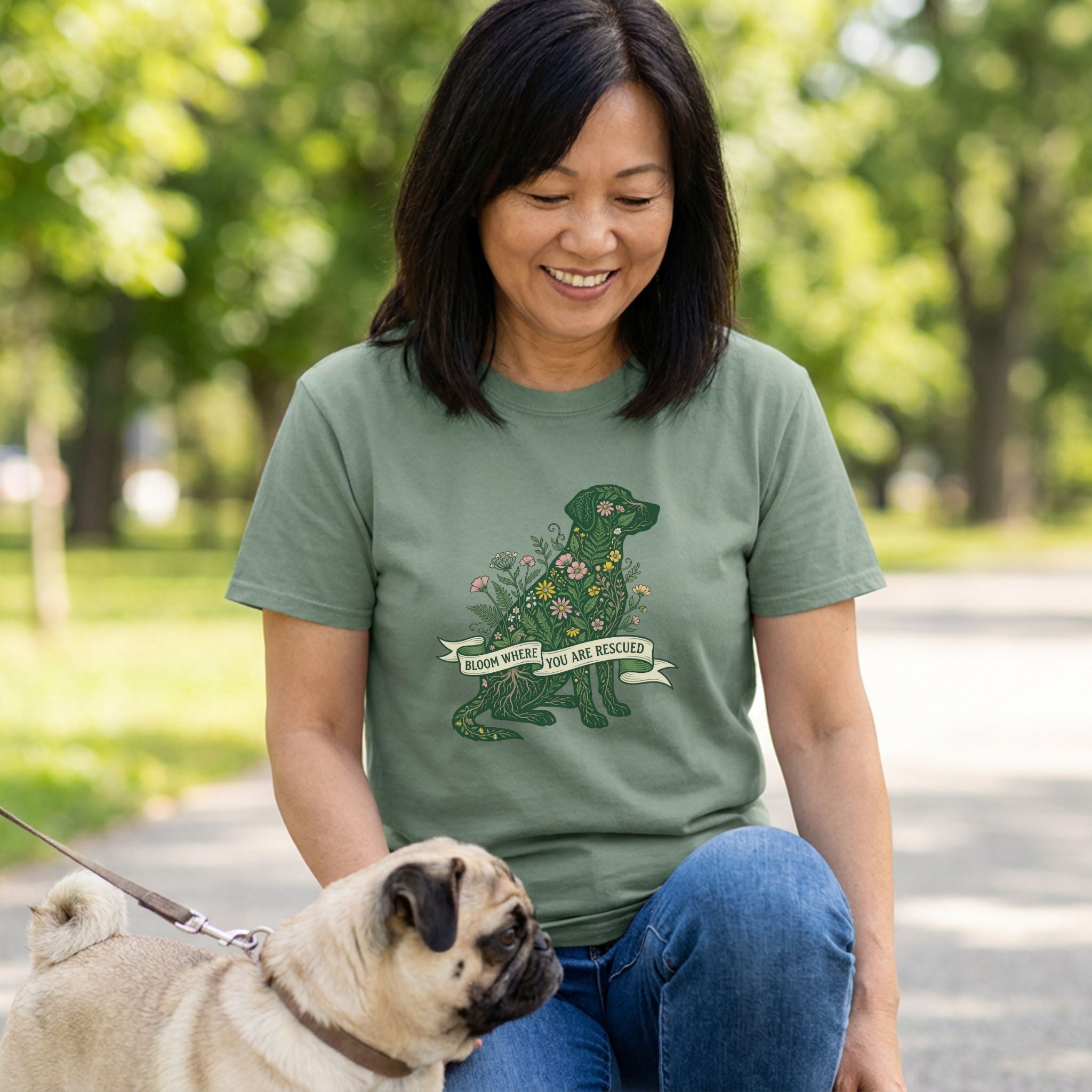 Woman in an olive green "Bloom Where You Are Rescued" t-shirt with a floral dog design, petting a pug.