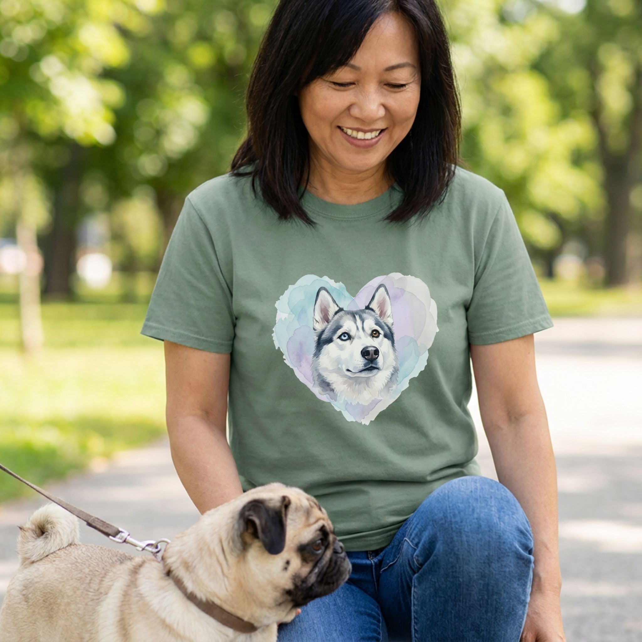Woman in an olive green Gildan Softstyle® tee with a watercolor husky heart design, petting a pug.