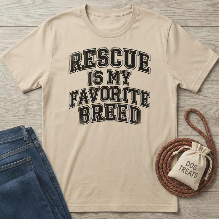 Beige cotton t-shirt with "Rescue Is My Favorite Breed" in distressed black text, next to jeans and dog treats.