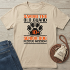Beige "Saving The Old Guard Senior Dog Rescue Mission" t-shirt with orange and black text, featuring a paw print.