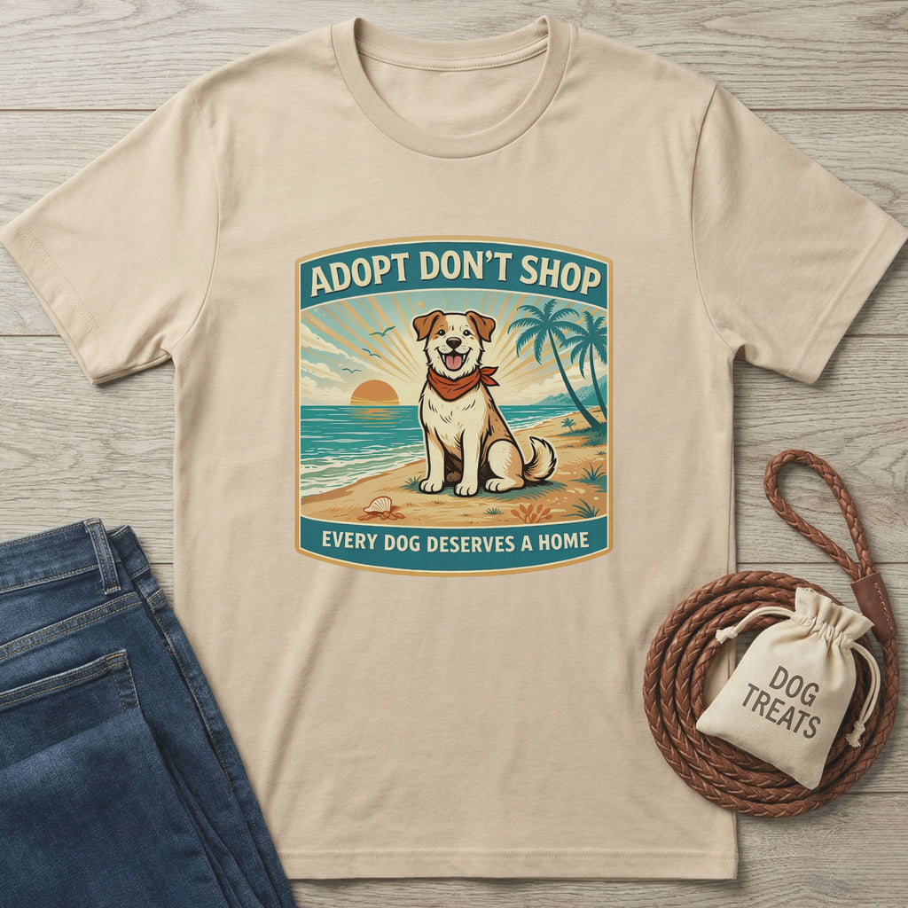 Beige "Adopt Don't Shop" t-shirt with a dog on a beach graphic, next to jeans and dog treats.