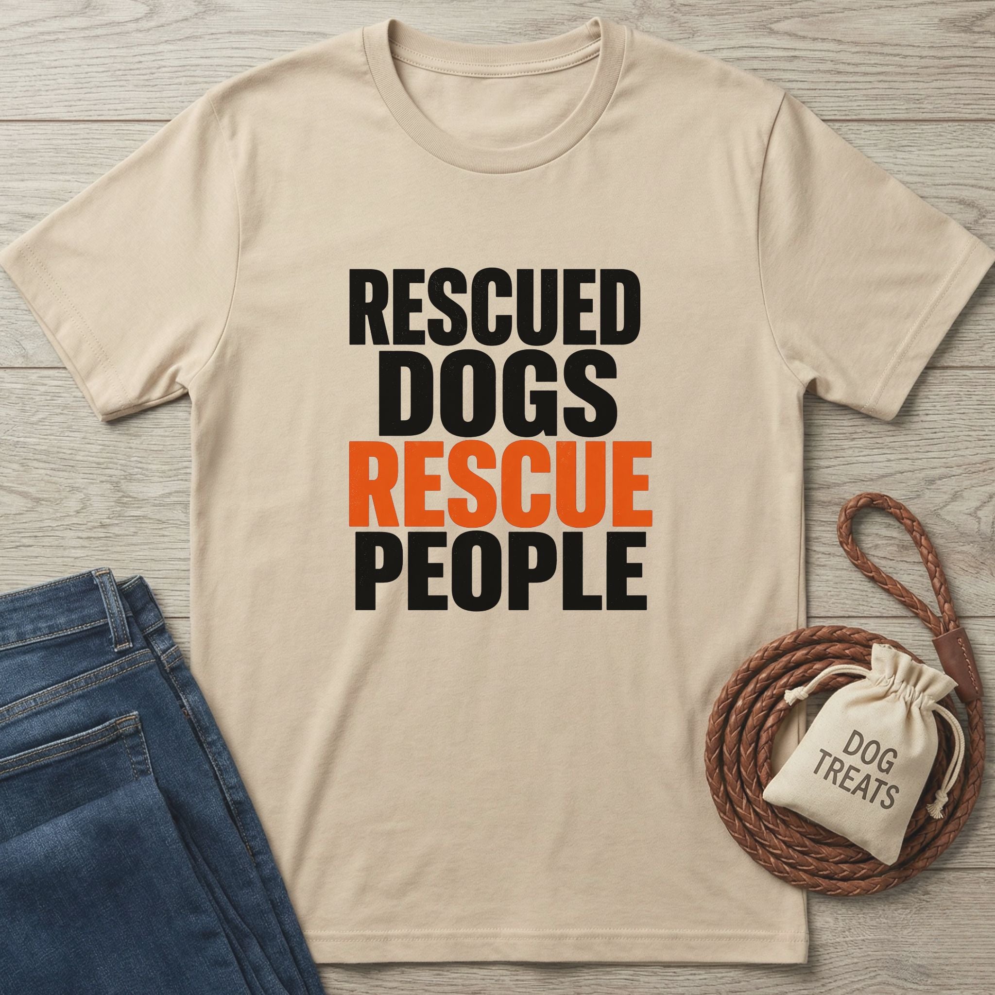 Light beige Gildan Softstyle® t-shirt with "RESCUED DOGS RESCUE PEOPLE" text, paired with jeans and dog treats.
