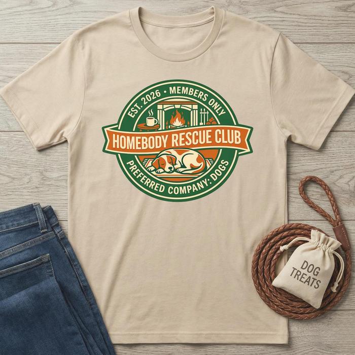 Beige Homebody Rescue Club T-shirt with green and orange logo featuring a sleeping dog, fireplace, and coffee.