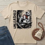 Beige "Unleashed" T-shirt with a jumping dog in an orange harness, next to jeans and dog treats.