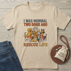 Sand Gildan Softstyle® t-shirt with "I WAS NORMAL TWO DOGS AGO RESCUE LIFE" and dog graphic.