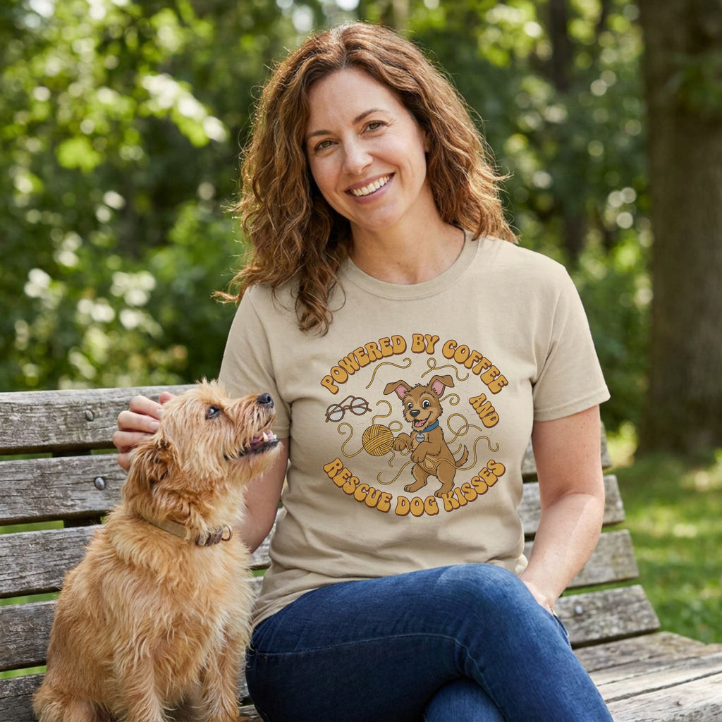 Woman in a tan Gildan Softstyle® tee with "Powered by Coffee & Rescue Dog Kisses" graphic, petting a dog.