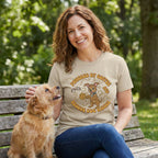 Woman in a tan Gildan Softstyle® tee with "Powered by Coffee & Rescue Dog Kisses" graphic, petting a dog.