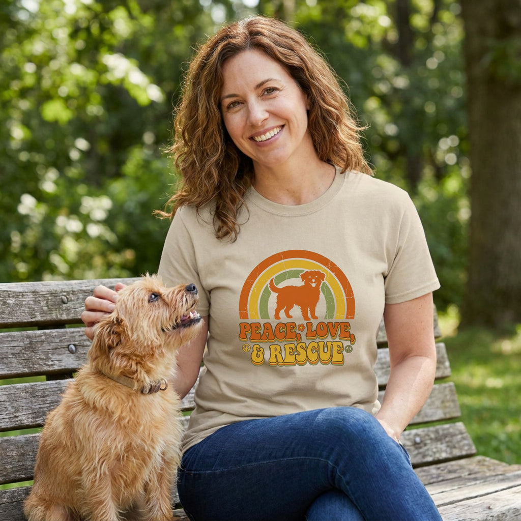 Woman in a tan Gildan Softstyle® tee with a "Peace, Love, & Rescue" dog and rainbow graphic, petting a small dog.