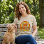 Woman in a tan Gildan Softstyle® tee with a "Peace, Love, & Rescue" dog and rainbow graphic, petting a small dog.