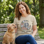 Woman in a tan "Dog Mom" Gildan Softstyle t-shirt with a floral dog portrait design, petting a small dog.
