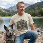 Man in a beige "Wild & Rescued" German Shepherd graphic tee with a blue heeler dog by a lake.
