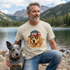 Man wearing a t-shirt with a dog graphic by a lake with mountains in the background