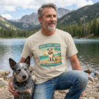 Man in a beige "Adopt Don't Shop" beach dog t-shirt with a blue heeler by a lake.