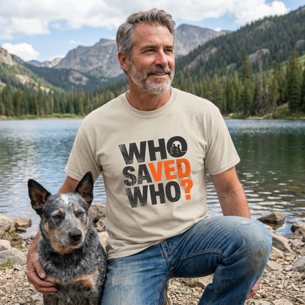 Man in a beige "Who Saved Who?" tee with a rescue dog by a lake and mountains.