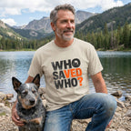 Man in a beige "Who Saved Who?" tee with a rescue dog by a lake and mountains.
