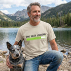 Man in a tan "Dog Hair Loading" t-shirt with a blue heeler dog by a lake.