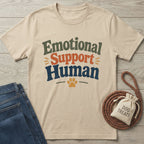 Beige "Emotional Support Human" t-shirt with a paw print, next to jeans and a "Dog Treats" bag.