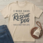 Beige cotton t-shirt with "I Work Hard So My Rescue Dog Has A Better Life" text, next to jeans and dog treats.
